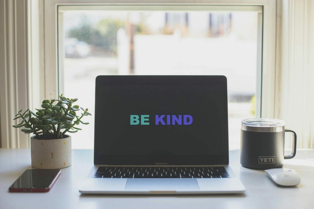 Laptop on a desk showing "Be kind" on the screen